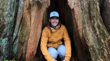 Emma crouches in the crevice of a tree trunk
