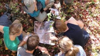 small group of people outdoors crouched over some sort of document