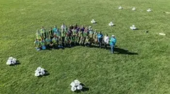 A group of people posing for a photo taken by a drone, they are standing on a grassy field
