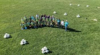 A group of people posing for a photo taken by a drone, they are standing on a grassy field