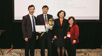 Four people standing in a line at a conference; man second from left holds an award he has received