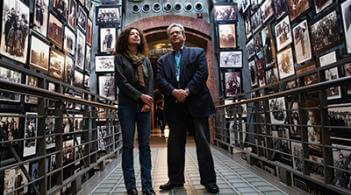 A hallway lined with pictures features two people standing together
