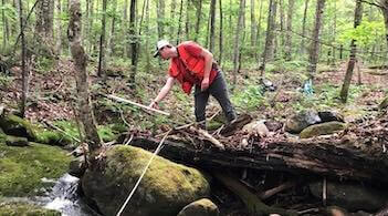 A scientist measures a log beside a stream