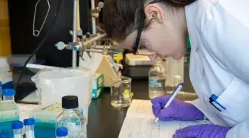 A student taking notes on a lab bench
