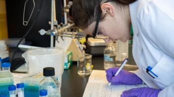 A student taking notes on a lab bench