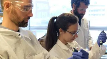 three researchers in lab coats working with pipettes