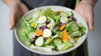 A bowl of fresh salad with sliced hard-boiled eggs is offered to the camera
