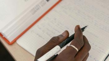 A Black college student pores over their notes next to an open textbook