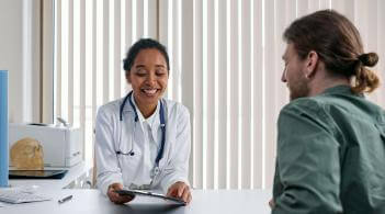 A copper-skinned college-aged woman in medical coat explains something from an iPad