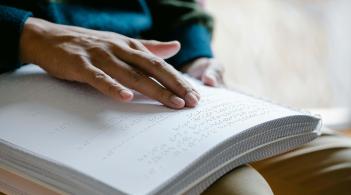 A copper-skinned hand reading a page of Braille text