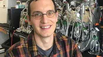 A man wearing glasses and a flannel smiles