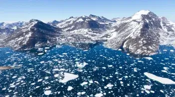A blue sea with ice chunks in it with mountains behind