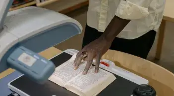 A Black student uses a magnifier to read text in an open book