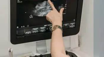 A medical tech off-screen points to something on an ultrasound