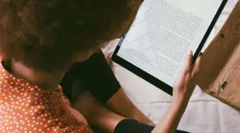 A Black student reads large text on a tablet while sitting cross-legged