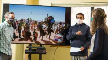 Three people stand by a big screen