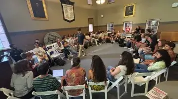 Students seated in a large circle in a historic classroom, engaged in a group discussion.