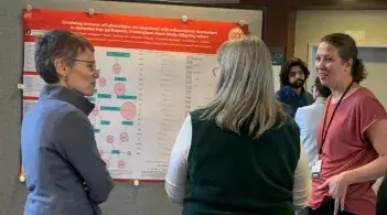 Three people standing in front of a poster discussing the research represented on the poster