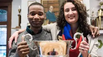 Two students smiling and holding a large trophy together.