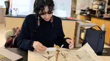 a young woman looking down at a pressed plant specimen in a lab