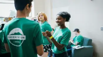 Students wearing matching orientation T-shirts chatting and checking in indoors.