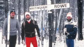 three men in winter cloths and skis standing in the forest