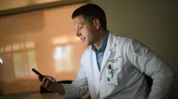doctor in white coat looking at a cell phone