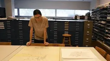 a person leaning over an outspread map in the library