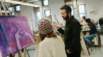 An art instructor talks with a student in a painting studio.