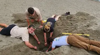 Students work together on a hands-on digging activity in the sand, using tools and measuring equipment.