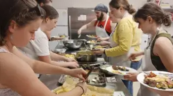Students cook and serve food together in a kitchen.