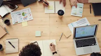 A group of laptops and planners with people, gathered around a table