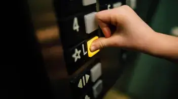 Hand pressing the Lobby button in an elevator