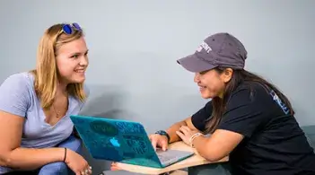 Two people sitting together, smiling and looking at a laptop.