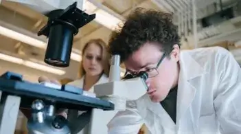 a man looking into a microscope while a woman looks on