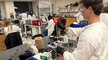 Student in a chemistry lab wearing safety gear and conducting an experiment at a lab bench.