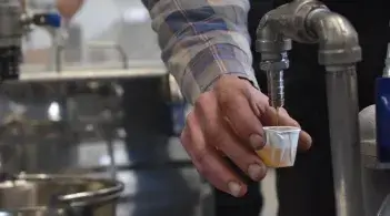 a hand filling up a paper cup of syrup from under a metal tap