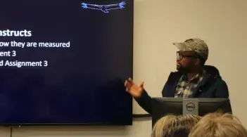 Person presenting next to a screen during a classroom lecture.