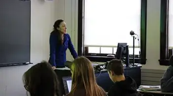 Instructor speaking to students in a classroom at the front of the room