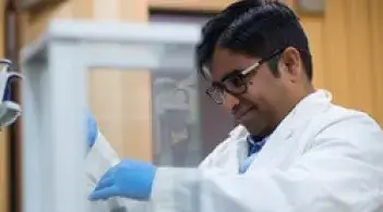 UVM Research Raju Badireddy in a lab wearing a white lab coat and blue gloves working with a test tube