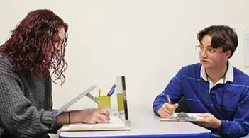 Two students discussing work while reviewing materials at a table.