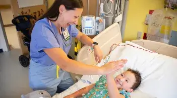 doctor in scrubs high fiving a young patient who is in a hospital bed