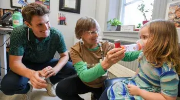 two people kneel beside a young child helping them use a respiratory aid
