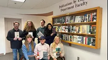 English faculty members posing with books in a library hallway.