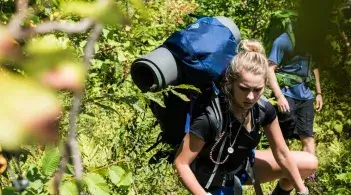 UVM student with backpack hikes on outdoor course in the woods