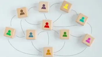 Nine wooden blocks, each displaying a different colored person icon, connected by looping lines to illustrate a network of interconnected people.