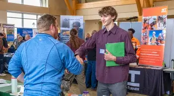 A student shakes hands with an industry recruiter at a technology career fair
