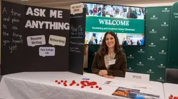 A vendor welcomes students beneath a sign that reads "Ask Me Anything"