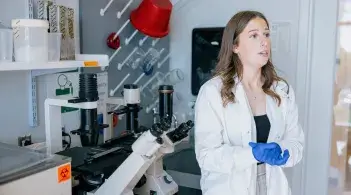 Student wearing a lab coat stands with lab equipment