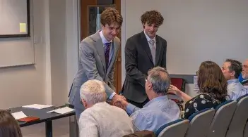 Students in professional attire shake hands with seated judges